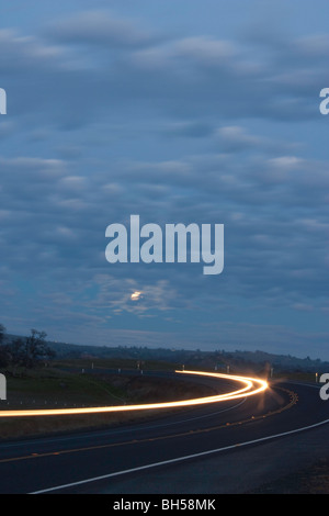 Une route de nuit avec la Lune se levant et des projecteurs et feux arrière des rayures sur la nuit des lunes périgée (au plus près de la terre) Banque D'Images