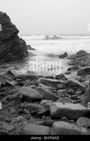 Estran rocheux avec surf se brisant sur une plage de Cornouailles en noir et blanc Banque D'Images