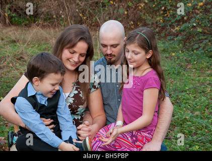 Cette heureuse famille caucasienne de quatre sont à la recherche de quelque chose sur little boy's shoe tandis que les enfants sont assis sur les genoux des parents. Banque D'Images