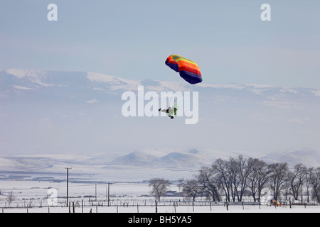 Powered parachute volant au-dessus des exploitations rurales. Multi coloured parachute aéronefs pour les loisirs et le sport. Montagnes en arrière-plan. Banque D'Images