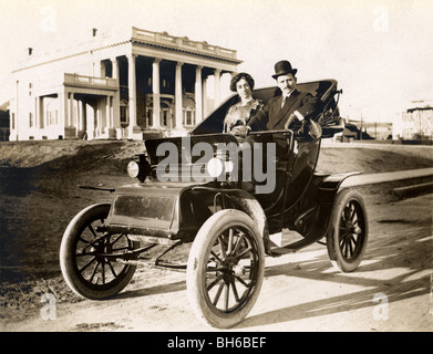 Couple au volant la voiture électrique en face de Mansion Banque D'Images