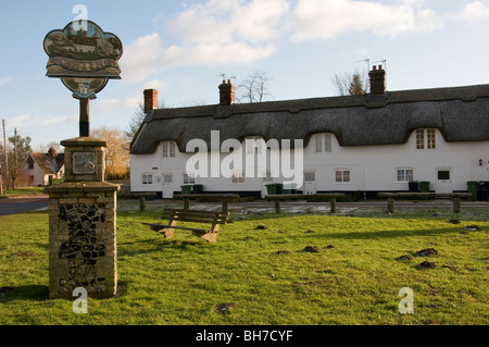 Le panneau du village de Weeting à Norfolk avec 'La ligne' cottages derrière. Banque D'Images