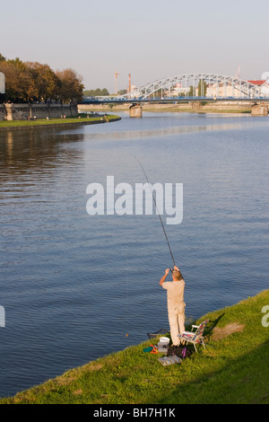 Pêche Homme vu dans soleil sur les rives de la Vistule avec pont pilsudski et podgorze derrière. Banque D'Images