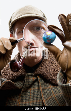 Un homme habillé comme Sherlock Holmes à la recherche à un petit monde à travers une loupe Banque D'Images