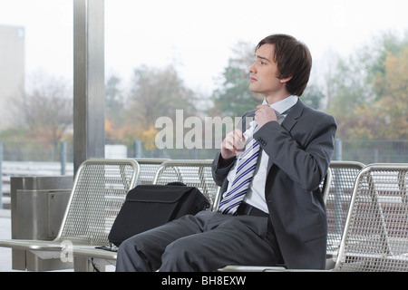 Businessman on bench, adjusting tie Banque D'Images