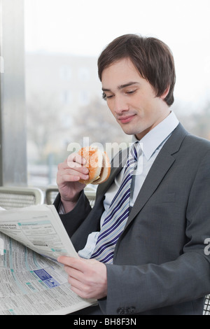 Businessman reading tout en mangeant Banque D'Images