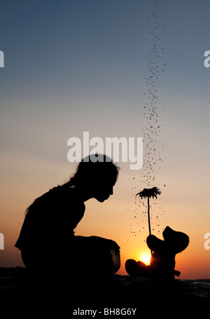 Indian girl et ours tient une fleur au coucher du soleil avec des gouttes d'eau. Silhouette. L'Inde Banque D'Images