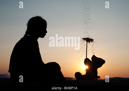 Indian girl et ours tient une fleur au coucher du soleil avec des gouttes d'eau. Silhouette. L'Inde Banque D'Images