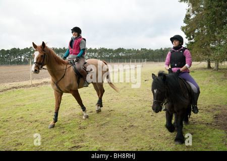 Deux adolescentes et leur cheval équitation poney entre forêt, la forêt de Thetford, Norfolk, UK Banque D'Images