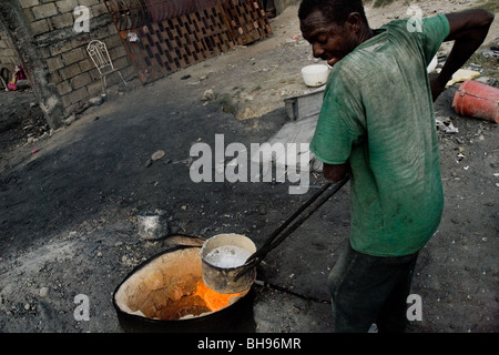 Un Haïtien fonctionne avec de l'aluminium fondu pour faire un pot de cuisine dans l'atelier de recyclage de l'aluminium à Port-au-Prince, Haïti. Banque D'Images