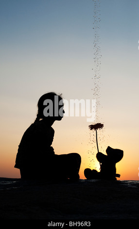 Indian girl et ours tient une fleur au coucher du soleil avec des gouttes d'eau. Silhouette. L'Inde Banque D'Images