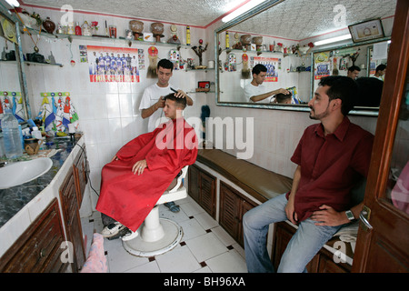 Petit salon de coiffure où un homme obtient une coupe alors que l'autre attend son tour. Banque D'Images