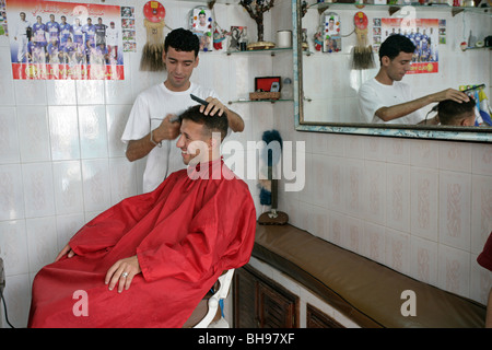 C'est un petit salon de coiffure où un homme obtient une coupe alors que l'autre attend son tour. Banque D'Images