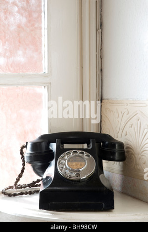 Un vieux téléphone en bakélite assis sur un coin de table dans une chambre. Banque D'Images