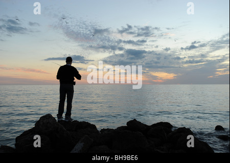 Pêcheur solitaire se tenait sur les rochers à l'encontre d'un spectaculaire coucher de soleil sur la plage de Naples Florida USA Banque D'Images