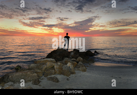 Pêcheur solitaire se tenait sur les rochers à l'encontre d'un spectaculaire coucher de soleil sur la plage de Naples Florida USA Banque D'Images