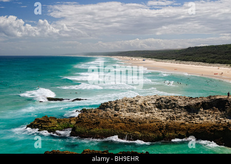 Point Lookout Beach North Stradbroke Island Australie / NORTH STRADBROKE ISLAND, Queensland, Australie — les nageurs naviguent sous le promontoire rocheux de point Lookout, le point le plus à l'est du Queensland. Cet affleurement accidenté forme une ancre géologique rare au milieu d'un paysage construit presque entièrement de sable accumulé sur des centaines de milliers d'années par les courants océaniques et le vent. La masse continentale environnante est Minjerribah - « île au soleil » - la maison traditionnelle du peuple Quandamooka, dont l'occupation de l'île est attestée archéologiquement il y a au moins 21 800 ans et par des années récentes Banque D'Images