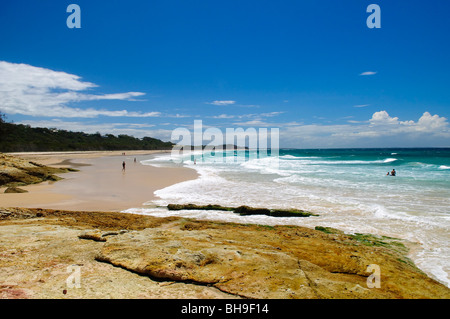 Cylinder Beach North Stradbroke Island Queensland Australie / NORTH STRADBROKE ISLAND, Australie — les nageurs et les marcheurs naviguent sur le rivage de Cylinder Beach, où les affleurements rocheux cèdent la place à une longue étendue de sable. Connue traditionnellement sous le nom de Minjerribah par le peuple Quandamooka, la masse continentale est la deuxième plus grande île de sable du monde, couvrant environ 106 miles carrés (275 kilomètres carrés). Ses vastes systèmes de dunes ont été formés par des centaines de milliers d'années de courants océaniques balayant les sédiments vers le nord le long de la côte du Queensland, fusionnant autour de l'éperon rocheux à point Lookout - th Banque D'Images