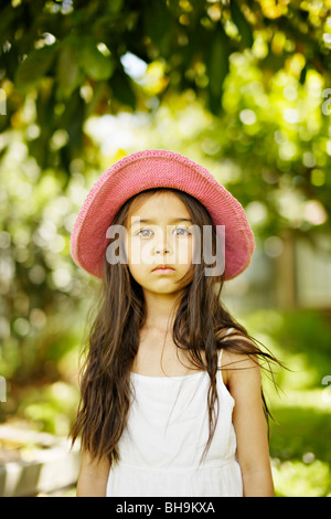 Fillette de six ans portant chapeau rose à l'extérieur dans un jardin Banque D'Images