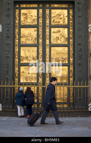 Un homme avec valise passe devant les portes en bronze (portes du paradis) de la Battistero Baptistère San Giovanni (Florence), Italie Banque D'Images