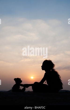Indian girl holding her teddy bears paw au coucher du soleil. Silhouette. L'Inde Banque D'Images