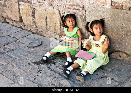 Jolie petite chambre lits jumeaux mexicains filles portent des expressions semblables, assis sur un trottoir et décider de la meilleure façon de faire face à l'écoulement des tacos Banque D'Images