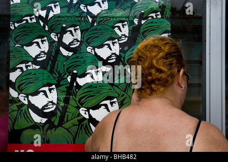 Une femme cubaine à la recherche à travers une vitrine couverte par l'affiche de propagande de Fidel Castro à Santiago de Cuba, Cuba. Banque D'Images