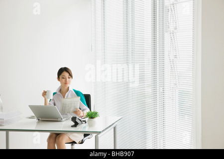 Japon, Osaka Prefecture, Businesswoman with coffee cup, journal de lecture à la suite Banque D'Images