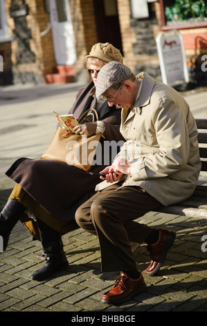 Homme âgé saisie des contacts dans son téléphone mobile comme son épouse de leur lecture de son carnet d'adresses, UK Banque D'Images