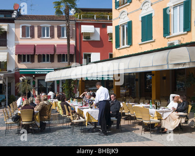 Milan, Lombardie, Italie. Waiter serving client à la terrasse d'un café avec vue sur le lac de Garde. Banque D'Images