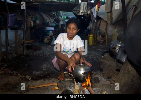 Jeune femme avec casserole sur feu ouvert prépare un repas au camp de personnes déplacées IDP bondé de familles sans-abri à Dili au Timor oriental Banque D'Images