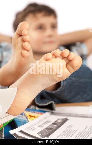 Portrait d'un écolier pieds nus avec ses pieds sur son bureau, attendant pour les vacances à venir Banque D'Images