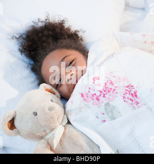 Mixed Race girl in bed with teddy bear Banque D'Images