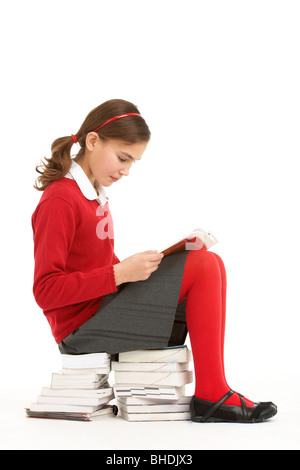 Étudiante en uniforme assis sur la pile de livres à lire Banque D'Images