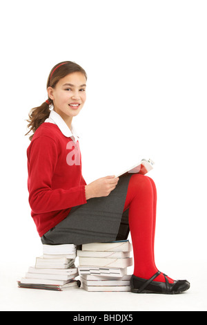 Étudiante en uniforme assis sur la pile de livres à lire Banque D'Images