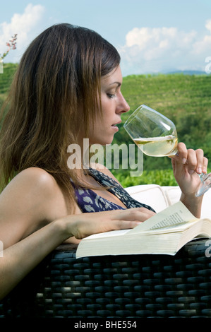 Young woman sitting on couch in vineyard boire le vin blanc et la lecture d'un livre Banque D'Images