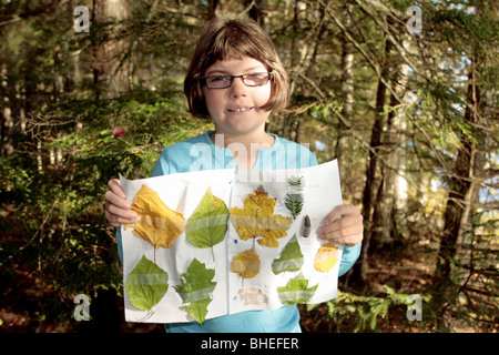 Une fillette de 8 ans enfant avec un projet scolaire sur l'identification des feuilles d'arbres Banque D'Images