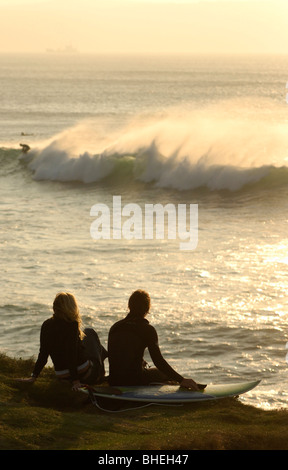 Young couple sitting on surf surf baord sur le bord de la falaise, regardant les vagues Banque D'Images