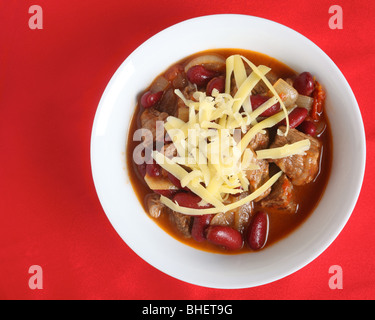 Un bol de chili au bœuf, garni de fromage, sur une nappe rouge avec espace pour un texte Banque D'Images