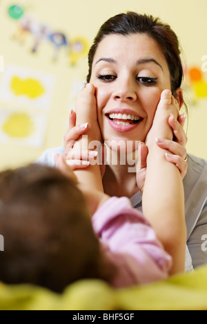 Maman jouant avec sa fille sur le lit et la tenue des pieds. La forme verticale Banque D'Images