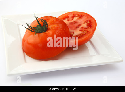 Grand, mûr, juteux, Rouge tomate boeuf bio coupé en deux moitiés, carré blanc sur plaque à fond blanc. Banque D'Images