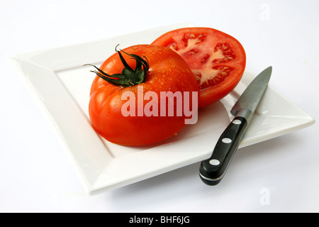 Grand, frais, rouge, juteuse, tomates mûres coupées en deux moitiés sur square plaque blanche avec couteau de cuisine, fond blanc. Banque D'Images