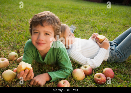 Mixed Race brother and sister laying in grass with apples Banque D'Images