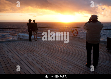 Jeune couple en regardant le coucher du soleil, sur le pont arrière en prenant des photographies, un paquebot de croisière, le Queen Mary 2, transatlantique, l'Atla Banque D'Images