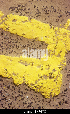 Détail du dessus de squidgy lignes doubles jaune vif avec l'extrémité barre sur route avec éclats tout juste visible à travers le sable Banque D'Images