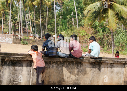 Regarder les garçons de village Jeux dans le terrain de jeu Village ouvert par assis sur le haut du mur.Une scène de village de Kerala, Inde Banque D'Images