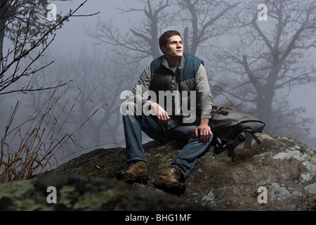 Un male hiker assis sur un rocher dans une forêt brumeuse Banque D'Images
