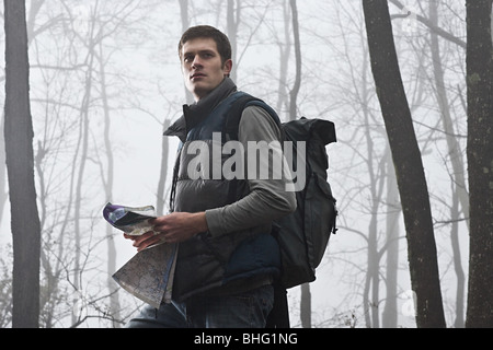 Un jeune male hiker holding une carte dans une forêt brumeuse Banque D'Images