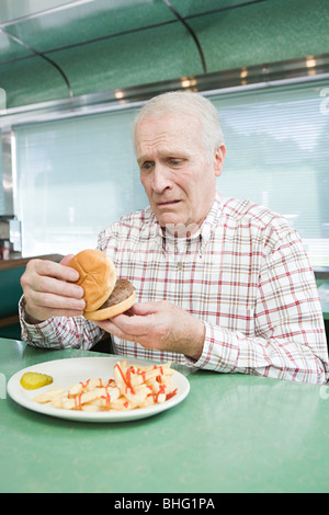 Inquiets old man looking at a burger Banque D'Images