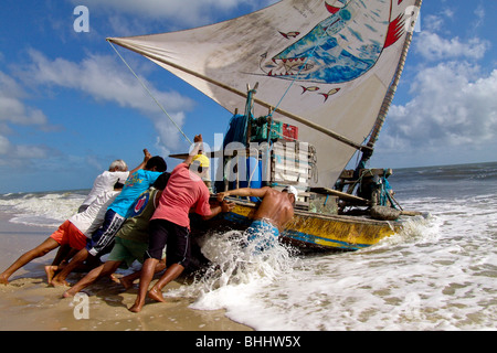 Les pêcheurs brésiliens en poussant leur bateau manuellement vers l'océan sur la plage de Prainha, au Brésil. Banque D'Images